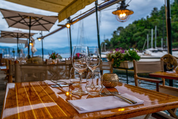 Empty outdoor restaurant table at sunset. Part of interior. Elegant restaurant table setting service for reception. View of a small local restaurant or trattoria in Italy