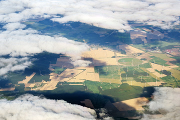 aerial view through the clouds to a wind farm with many wind turbines in an agricultural landscape