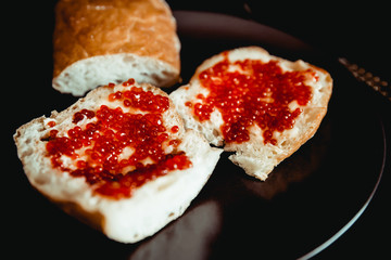 Sandwiches of white Fresh bread with butter and red caviar on a plate. Dark background