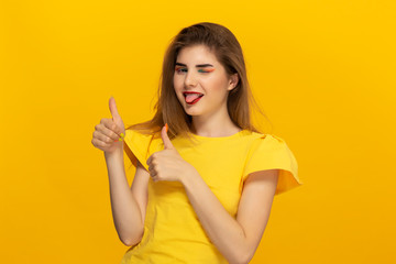 Close-up portrait of a beautiful young girl expressing approval with thumb up gesture isolated over yellow background.