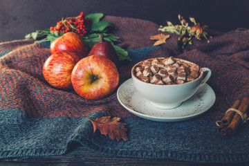 Autumn, fall leaves, hot cup of coffee with marshmallow and a warm scarf on wooden table background. Seasonal, morning coffee, sunday relaxing and still life concept.