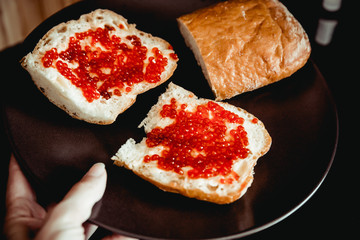 Sandwiches of white Fresh bread with butter and red caviar on a plate. Dark background
