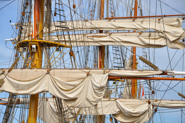 Masting of big wooden sailing ship, detailed rigging with sails with blue sky. Concepts: regatta, yachting, sailing