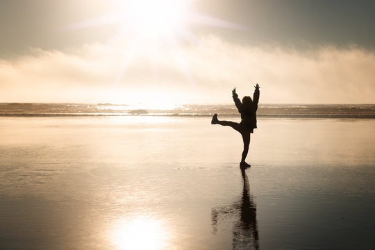 A silhouette of a little child dancing on an ocean beach on sunset background 