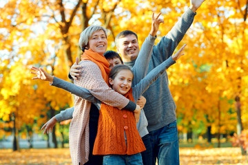 Happy family posing, playing and having fun in autumn city park. Children and parents together having a nice day. Bright sunlight and yellow leaves on trees, fall season.