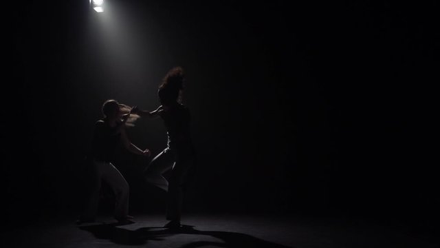 Two females practicing capoeira in darkness under spotlight in studio. Slow motion.