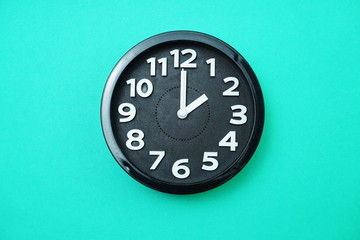 black round clock showing two o'clock on blue background