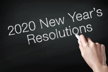 Hand holding a chalk and writing 2020 new year resolutions