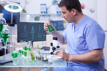 Side view of young scientific man holding a green solution in his research lab