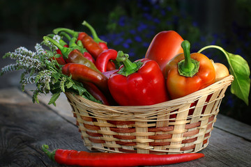  Wicker basket with different types of pepper, onions, garlic and sprigs of mint on a wooden background
