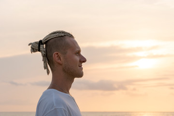 Silhouette of a young guy with dreadlocks on his head near sea during sunset. Close up portrait