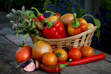 Wicker basket with sweet pepper, hot pepper, tomato, onion and garlic on a wooden background