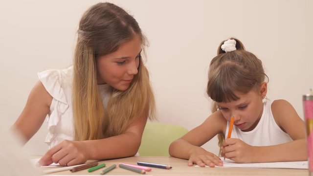 Teenage girl helping her little sister in drawing during psychological session. Picture interpretation technique usage