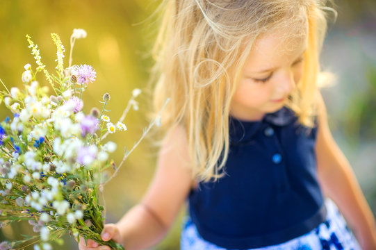 lovely cute little girl playing outdoors at sunset, holding a bouquet of wildflowers and walking on the field, happy childhood