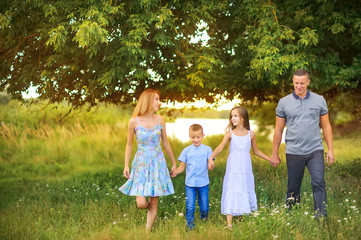Naklejka na ściany i meble portrait of a happy family outdoors, holding hands walk in the park at sunset, the family spends time together