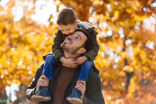 Happy father and little son playing and having fun outdoors over autumn park background