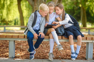 school friends, schoolchildren sitting on a bench in the park use a tablet, social media communication