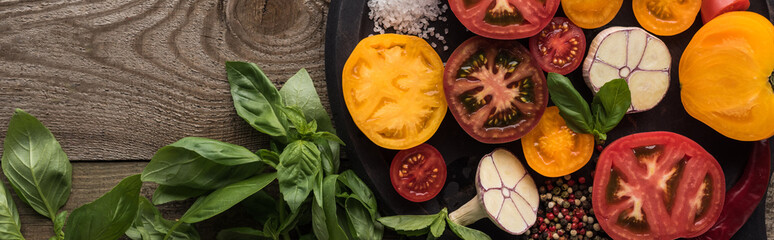 panoramic shot of tomatoes, garlic, chilli pepper, salt and pepper on pizza pan near spinach on wooden table