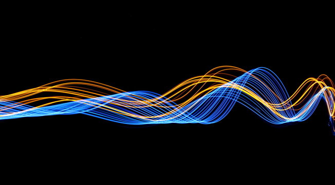Long exposure, light painting photography.  Vibrant streaks of electric blue and metallic gold color, against a black background.