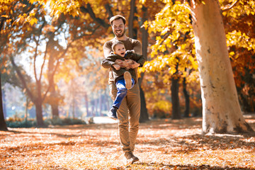 Happy father and little son playing and having fun outdoors over autumn park background