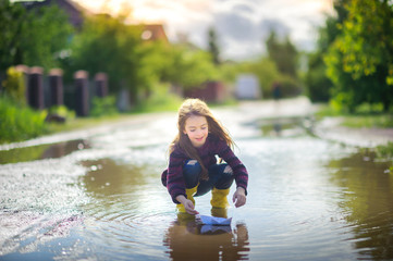 cute little girl in yellow boots plays in a puddle with a wooden boat, childhood, autumn concept