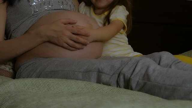 The daughter hugs and kisses the pregnant mother's stomach.