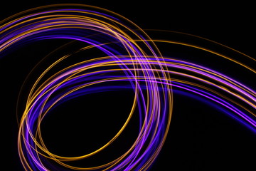 Long exposure, light painting photography.  Vibrant abstract streaks of neon pink and gold color against a black background.