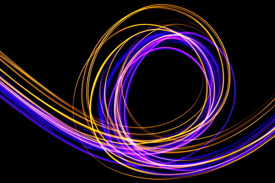 Long exposure, light painting photography.  Vibrant abstract streaks of neon pink and gold color against a black background.