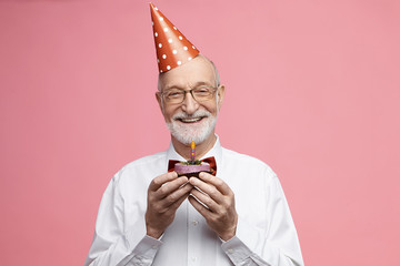 Attractive happy retired Caucasian male wearing bow tie, glasses and cone hat celebrating his 80th...