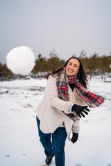 Fototapeta na wymiar Woman dressed in a coat, smiling because she threw a snowball at the camera - Vacation concept