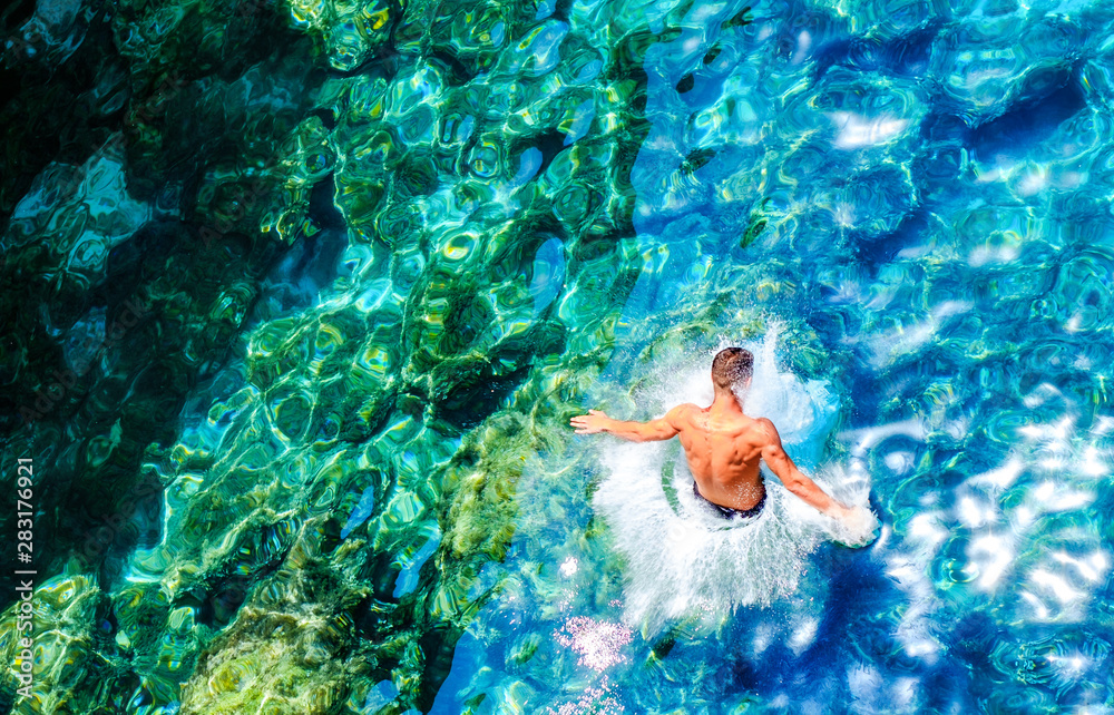 Wall mural a young man jumps into the turquoise water