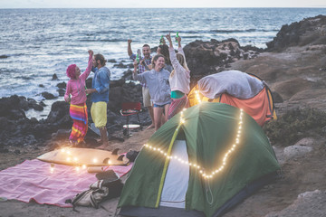 Happy friends doing bbq picnic camping in the desert after sunset - Young people dancing and...