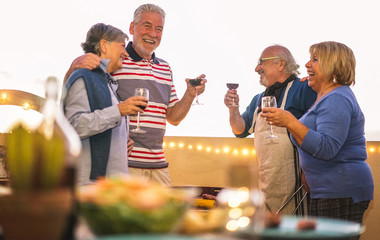 Senior friends having fun drinking wine at barbecue dinner in terrace outdoor - Mature people dining and laughing togheter - Joyful elderly lifestyle and friendship concept - Focus on right man face