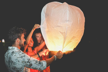 Happy friends lighting sky lantern on the beach at night - Young people having fun on floating lamps festival - Travel, vacation and fest concept - Focus on left man face