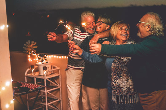 Group Of Senior Friends Celebrating Birthday With Sparkler Fireworks On Patio Terrace - Happy People Having Fun After Dinner In Summer Season  - Family And Holidays Concept - Focus On Right Woman Face