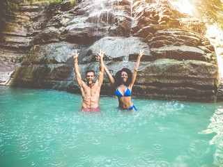 Travel influencer couple having fun under waterfalls river - Young people swimming inside emerald water lagoon - Summer, new trendy jobs concept and friendship concept - Focus on guys faces