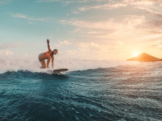 Fit female athlete surfing at sunset - Surfer woman performing outdoor inside ocean - Extreme sport, travel, healthy lifestyle, adventure and vacation concept - Focus on her body - obrazy, fototapety, plakaty