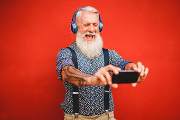 Senior hipster man using smartphone app for creating playlist with rock music - Trendy tattoo guy having fun with mobile phone technology - Tech and joyful elderly lifestyle concept - Focus on face