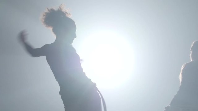 Muscular girls practicing capoeira in ray of spotlight in studio.