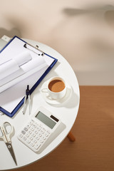 Top view of coffee notebook empty page, calculator, coffee cup scissors on white table