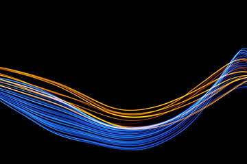 Long exposure, light painting photography.  Vibrant streaks of neon blue and gold color against a black background.