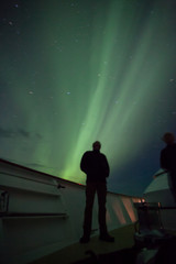 Obraz premium Beautiful aurora borealis, northern lights turn the night sky green over this ship as a man gazes up