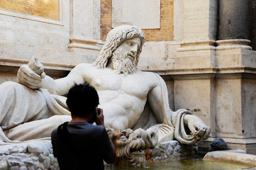 Marphurius or Marforio talking statues of Rome with an asian visitor taking a photo. Rome, Italy