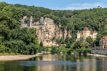 Fototapeta na wymiar La Roque Gageac, one of France's most beautiful villages by the Dordogne River, backed by a steep hill / cliff, Malartrie Castle in the background. Canoeing on the river. Travel France.