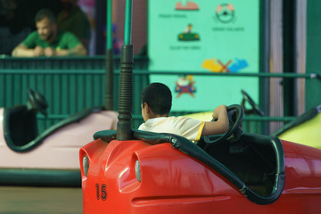 Boy riding on the bumper car / dodgems.  Flat ride which draw power from the floor and ceiling and...