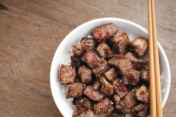 Homemade Bowl of Diced Beef Steak with rice Japanese style on wooden table.