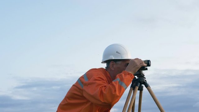 skilled surveyor in orange jumpsuit works with dumpy level