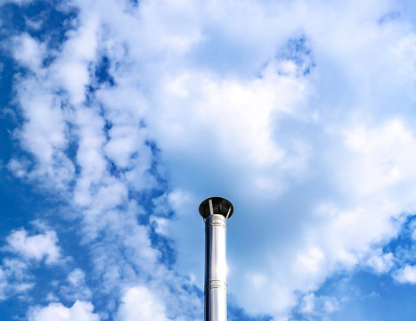 Stainless steel chimney in front of a bright blue sky with clouds.