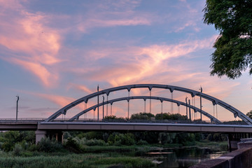 Large steel bridge over the river against a dramatic cloudy sky in Brest, Belarus, at sunset in summer. Architecture and nature in one picturesque landscape