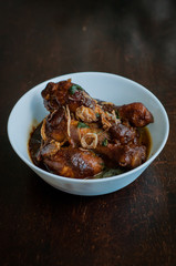 Malaysian dish of Ayam Masak Kicap or deep fried chicken in black soy gravy in a white bowl.